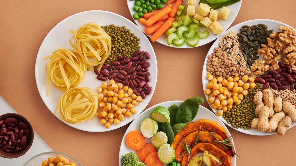 A vibrant mix of legumes, vegetables, nuts, and pasta arranged on white plates showcasing a balanced, healthy diet.