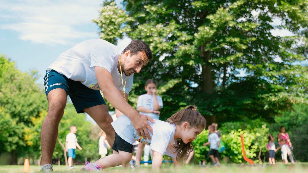 Children exercising with instructor outdoors, enjoying physical education in summer park setting.